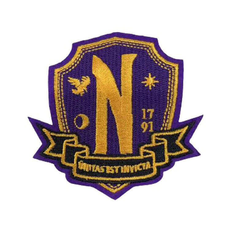 Nevermore Academy crest patch from Wednesday Addams Welcome Kit, featuring a purple and gold design with symbols and motto.